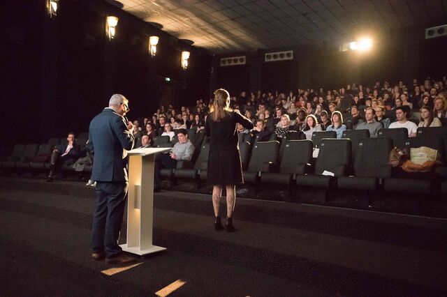 Een persoon die iets voorleest samen met iemand die de tekst in gebarentaal doet, voor het publiek in de cinemazaal